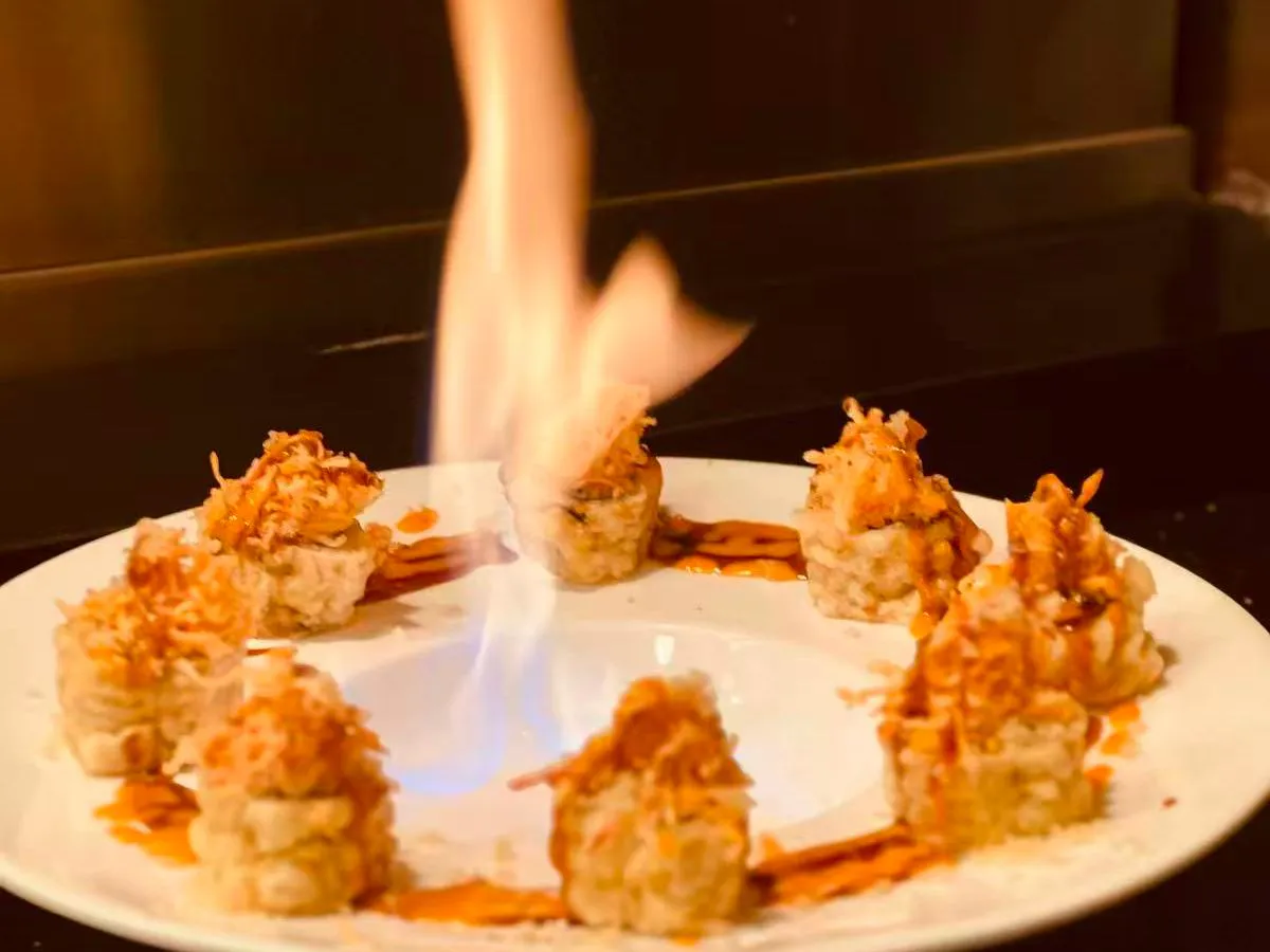 Flaming sushi rolls on white plate with crispy toppings and drizzled brown sauce
